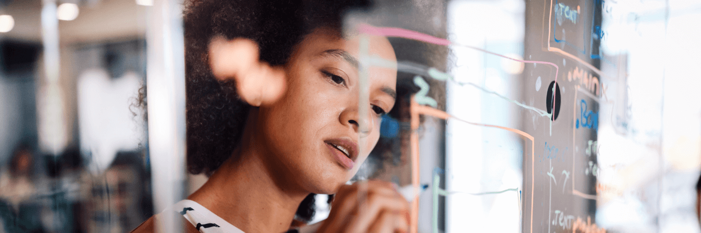 Woman writing with a colored marker on a glass board